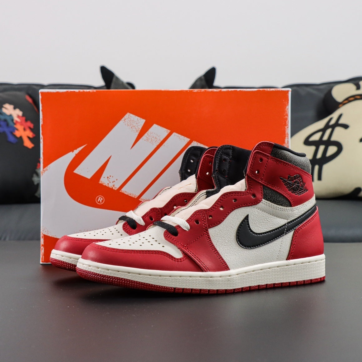 Air Jordan 1 Retro High OG Lost and Found. Red and white sneakers with black accents on a dark surface, with an orange Nike box in the background. 