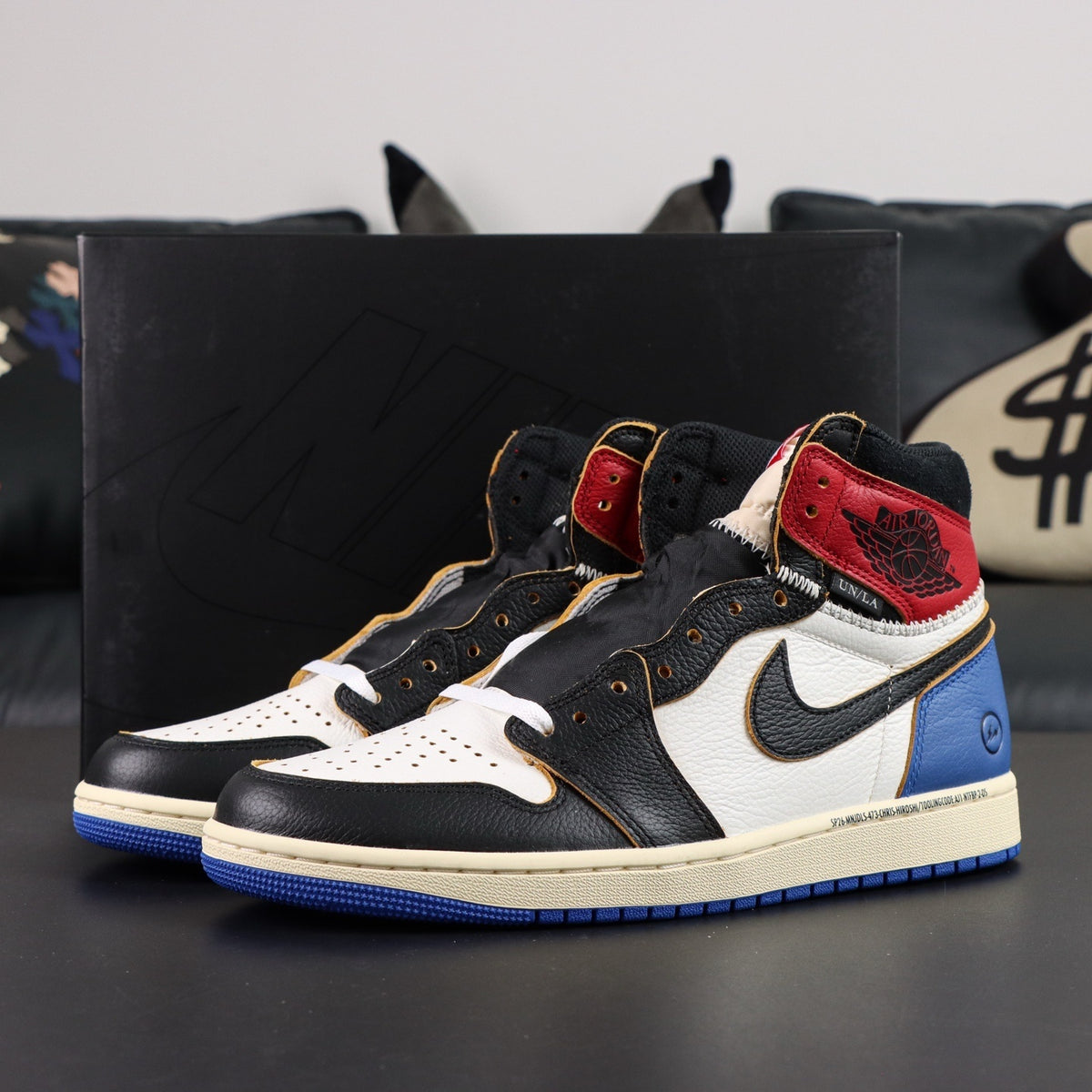 Black, white, red, and blue sneakers with a prominent Nike logo on a dark surface. Air Jordan 1 Retro High OG SP Fragment x Union LA Varsity Red Sport Royal