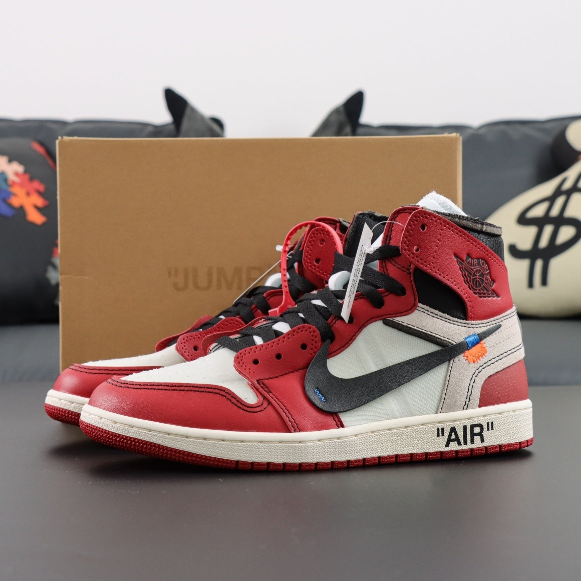 Red and white sneakers with black accents on a gray surface, with a brown box labeled Jumpman in the background.
Air Jordan 1 x Off-White Retro OG High Chicago