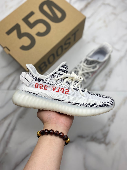 White and black sneaker with red text held by a hand, with a cardboard box labeled '350 Boost' in the background.